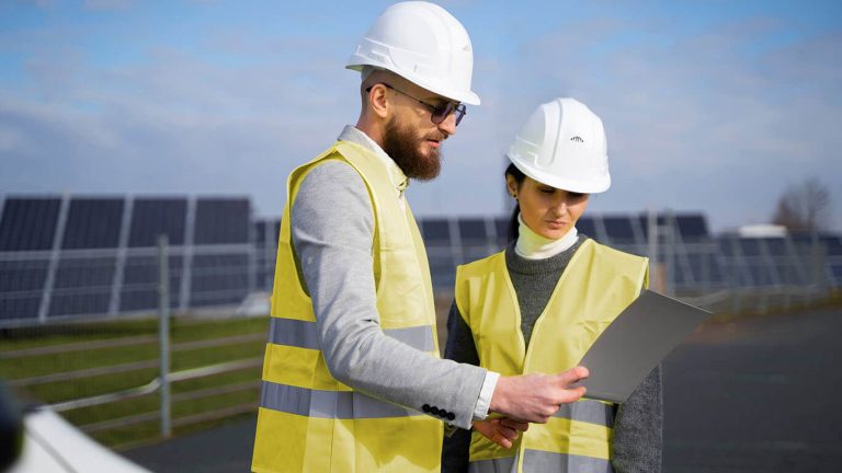 Two engineers in safety gear reviewing plans at a solar farm